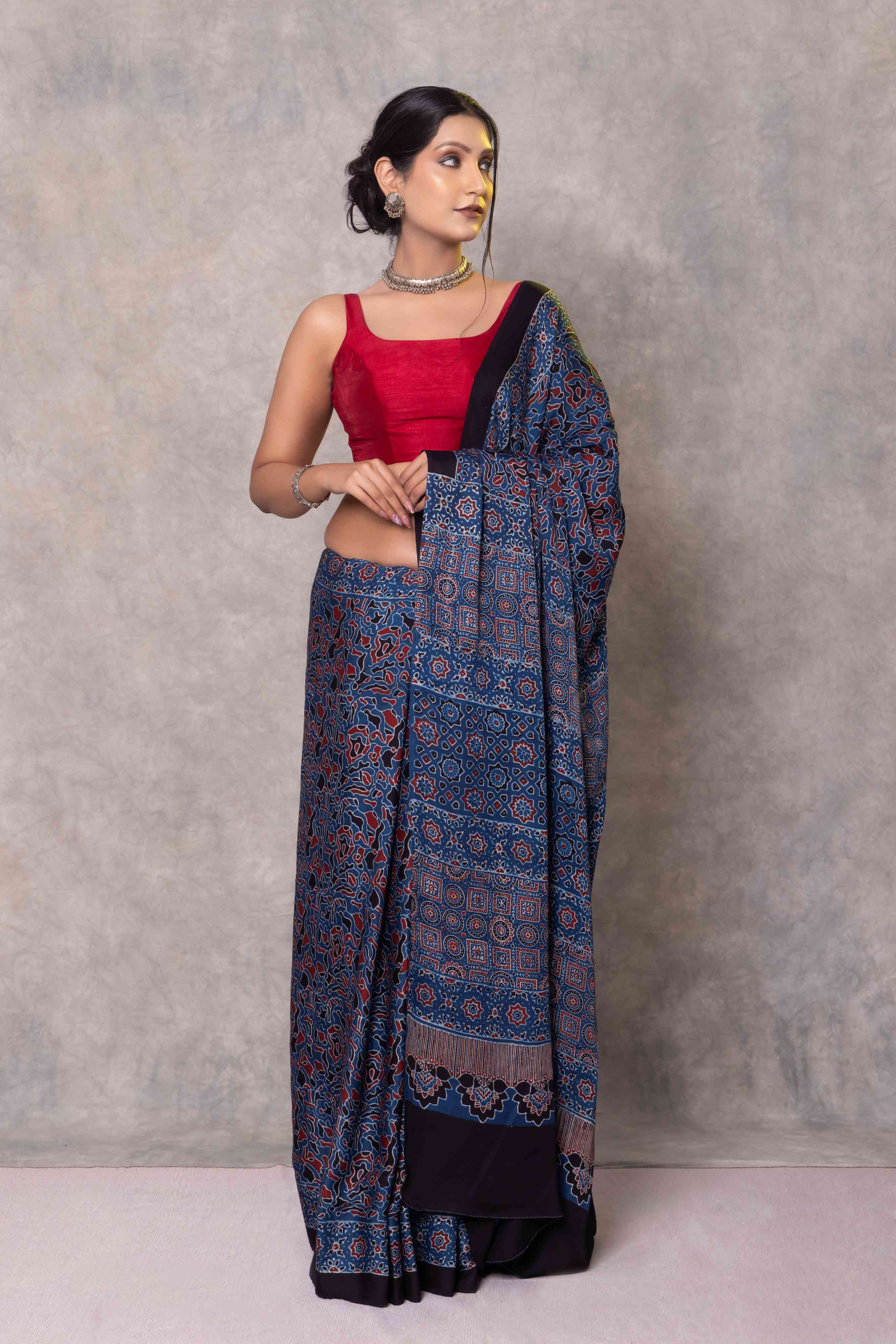 Woman wearing a blue patterned saree with a red blouse against a gray background