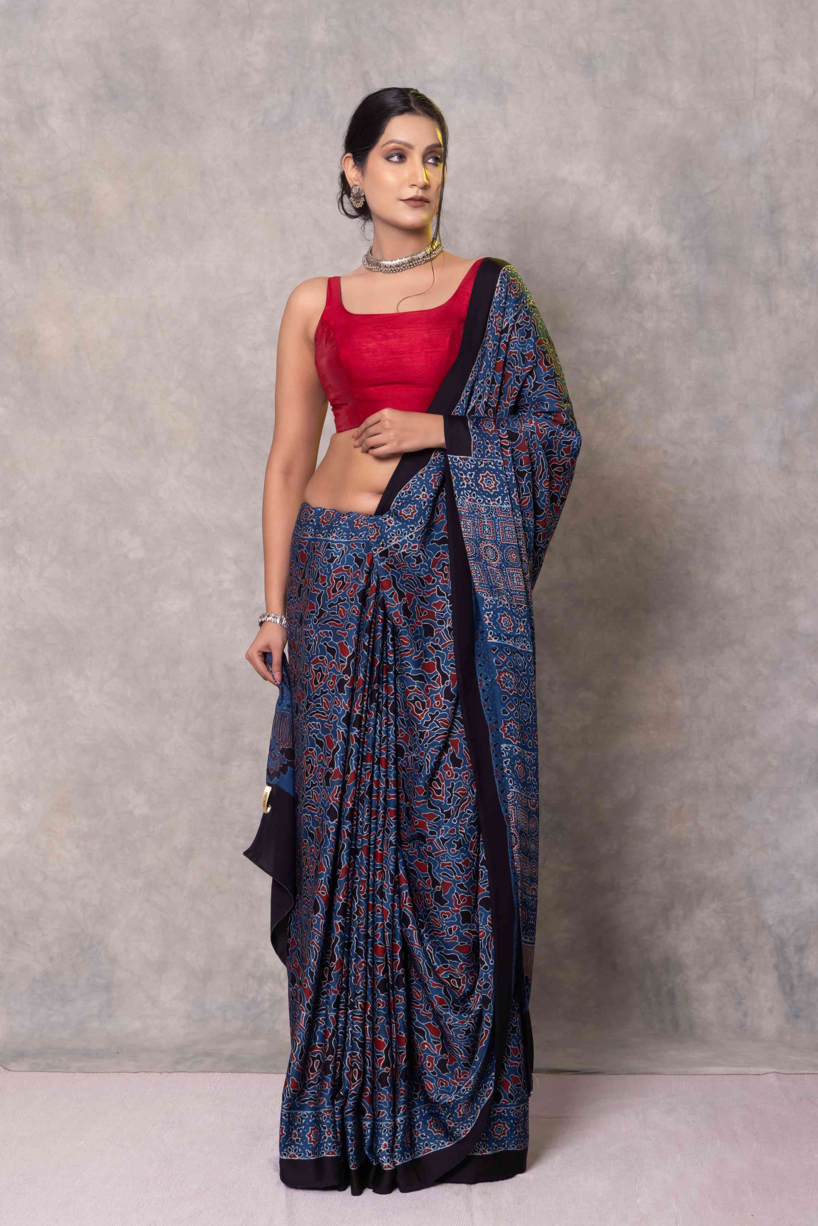 Woman wearing a blue saree with a red blouse against a gray background
