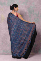 Woman wearing a black and blue patterned saree against a light purple background