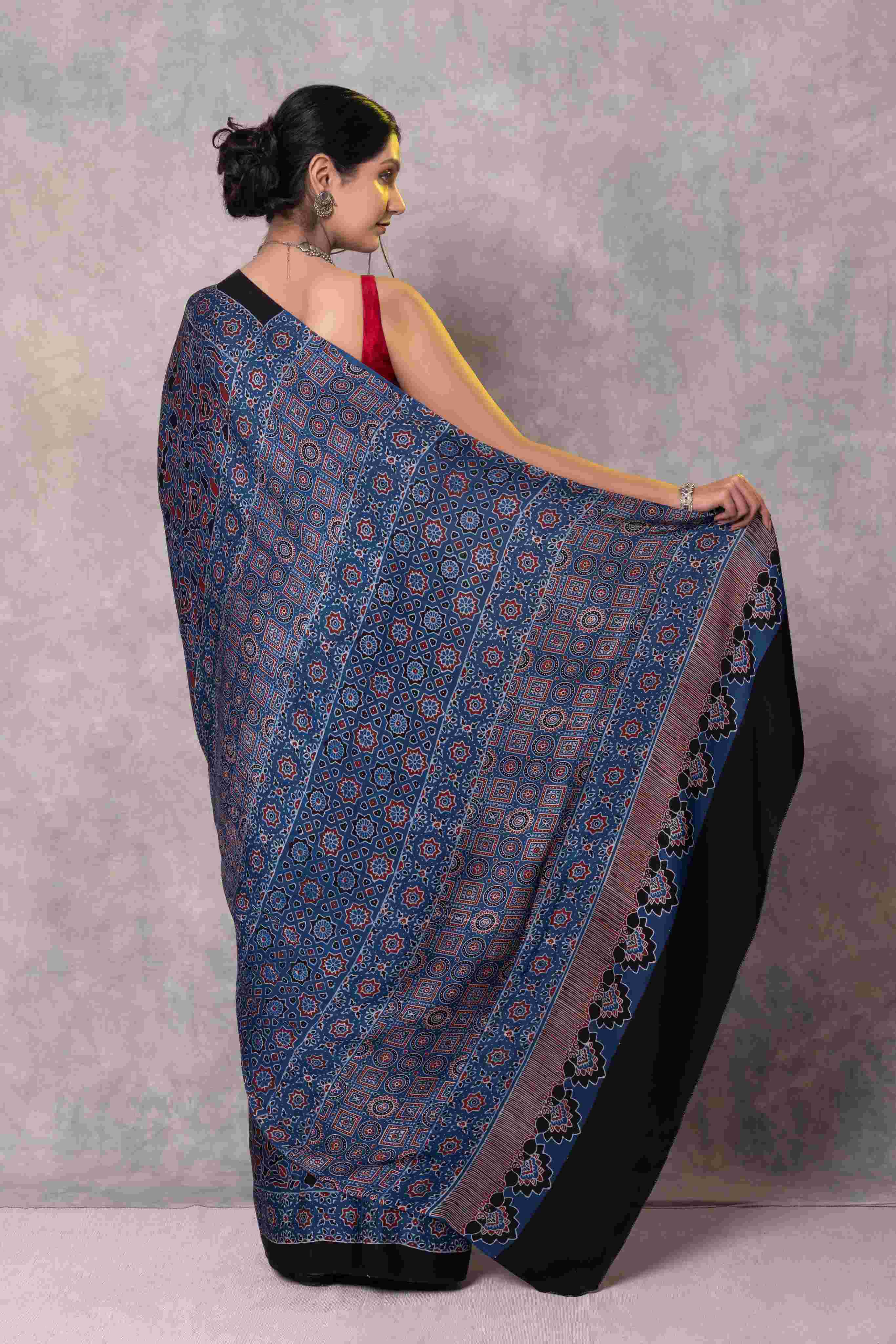 Woman wearing a black and blue patterned saree against a light purple background