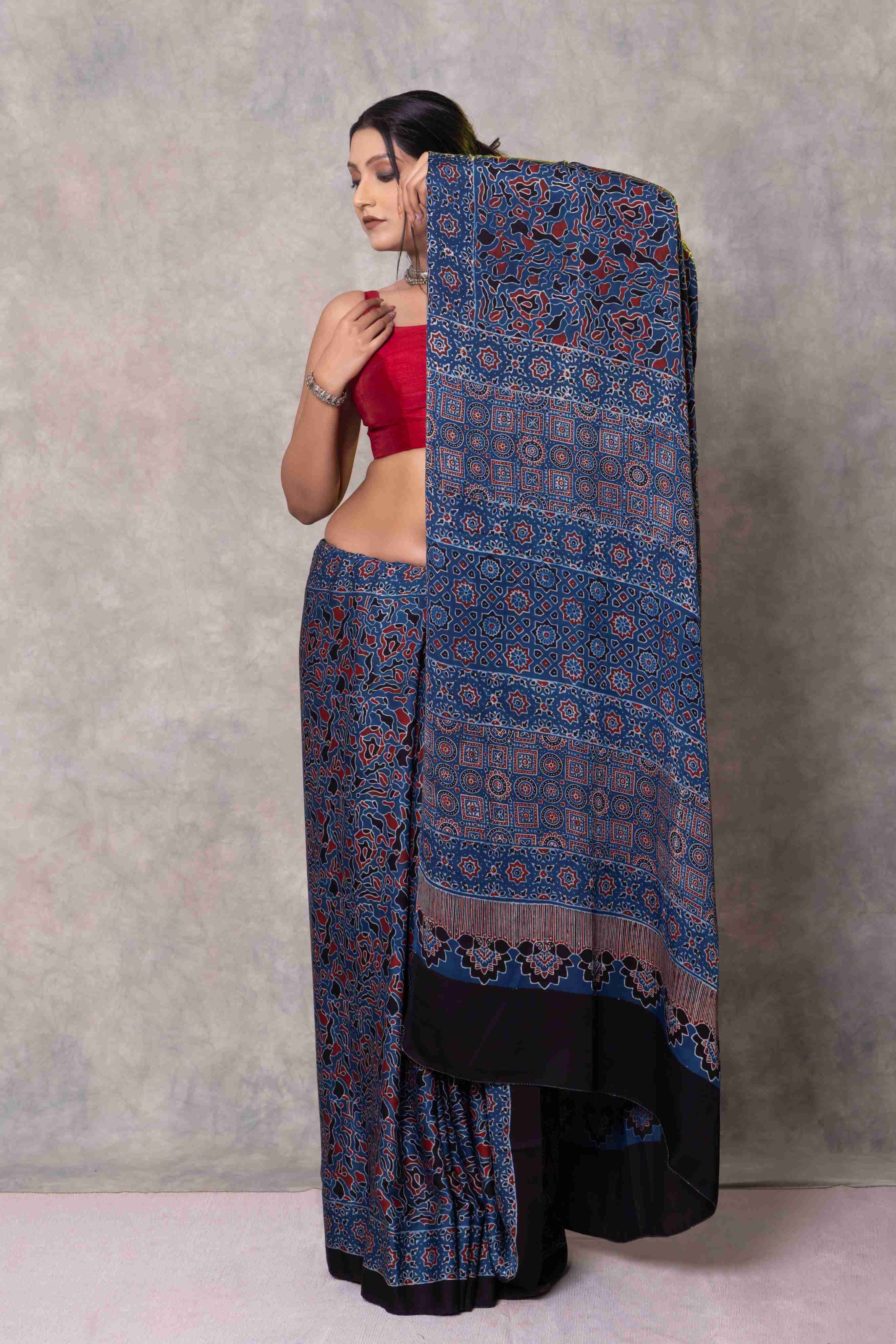 Woman wearing a blue patterned saree with a red blouse against a gray background