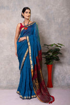 Woman wearing a blue saree with red and gold border against a gray background