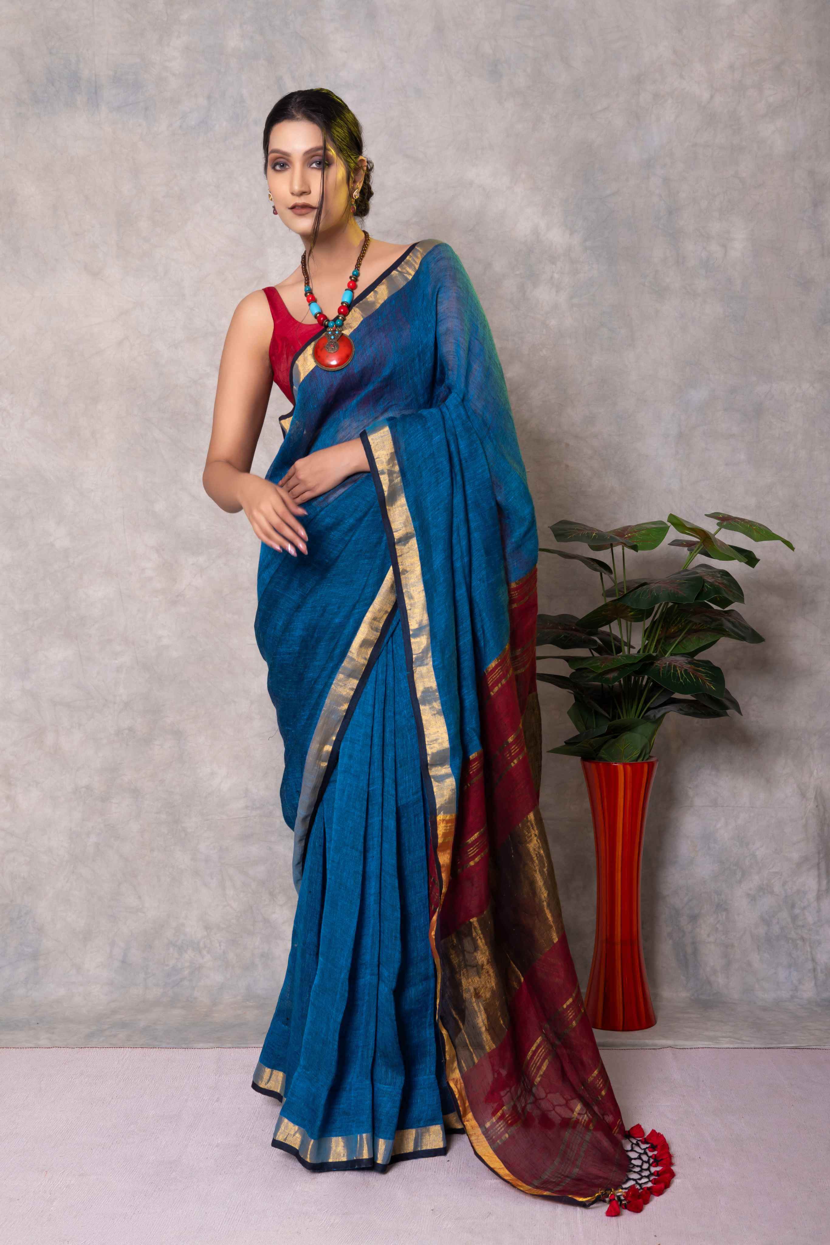 Woman wearing a blue saree with a red blouse against a gray background