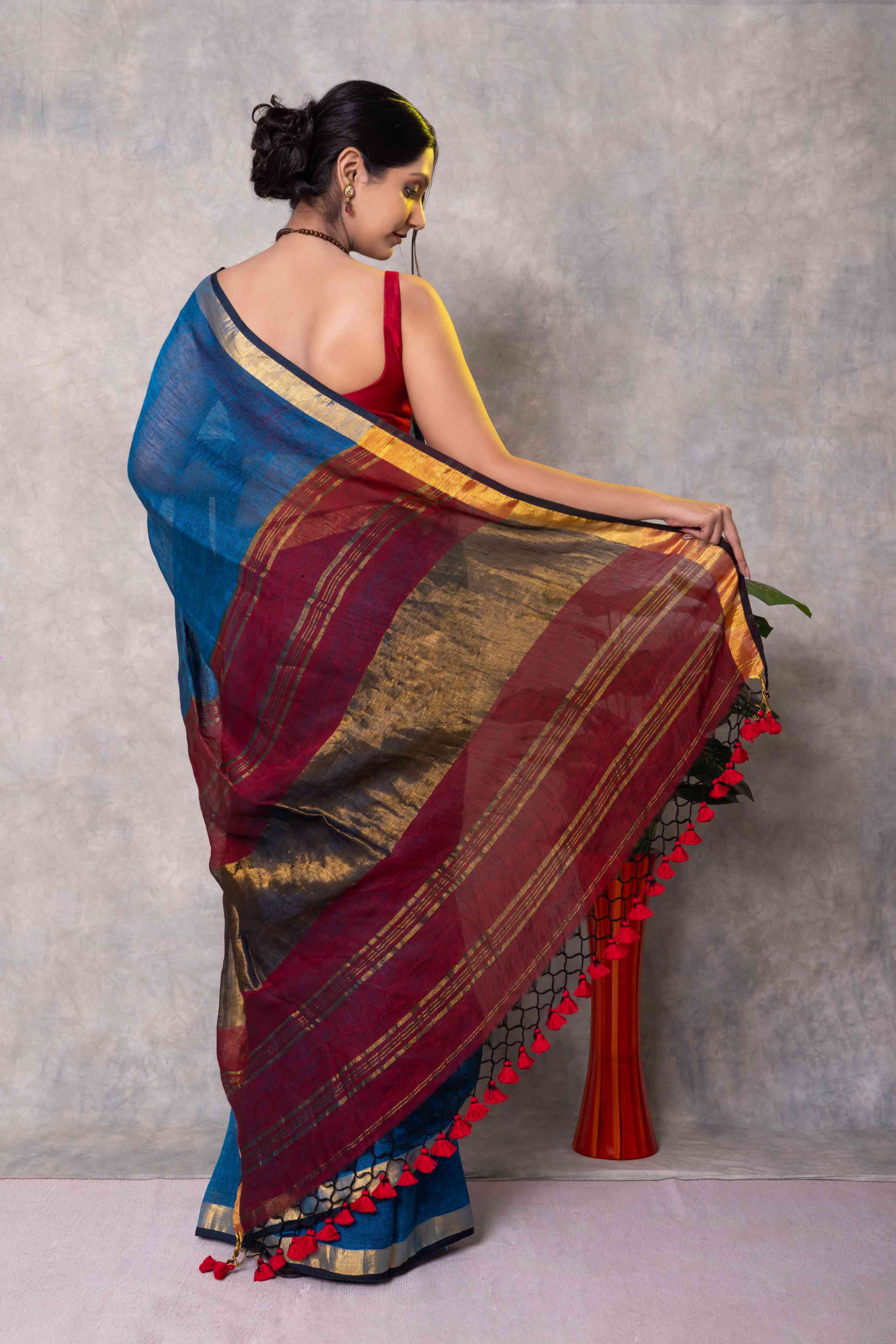 Woman wearing a traditional saree with a blue and red design against a gray background