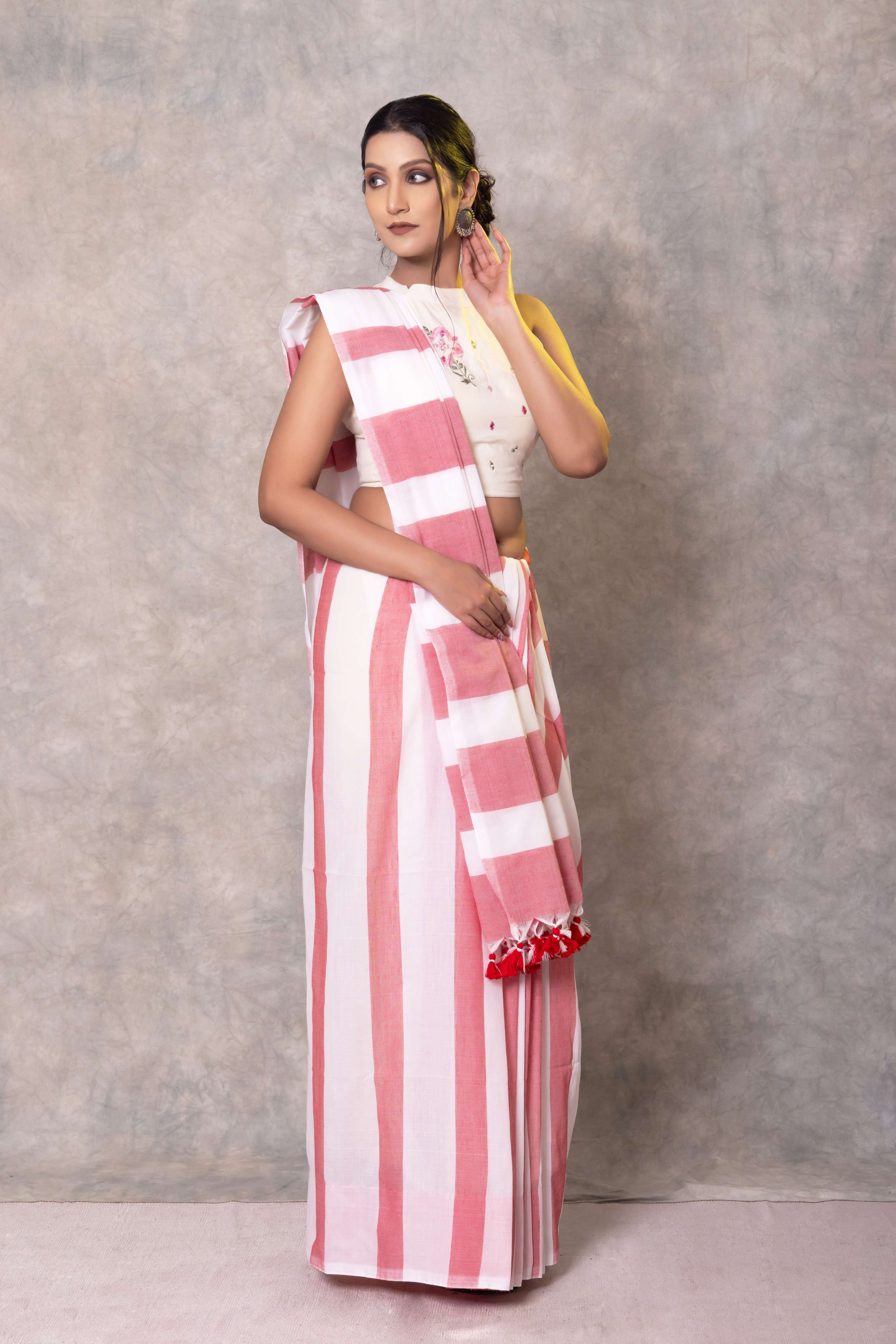 Woman wearing a pink and white striped saree with a yellow blouse against a gray background