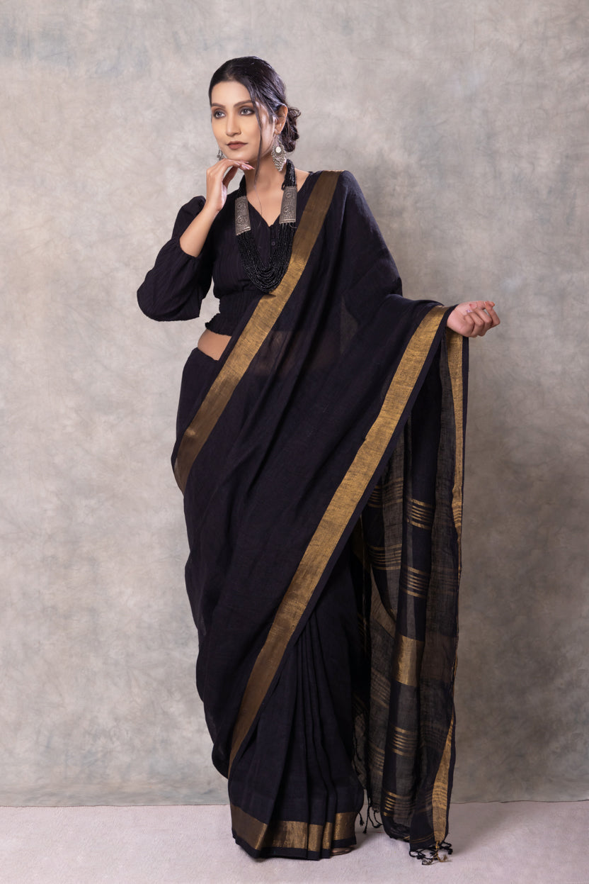 Woman wearing a black saree with gold border against a gray background
