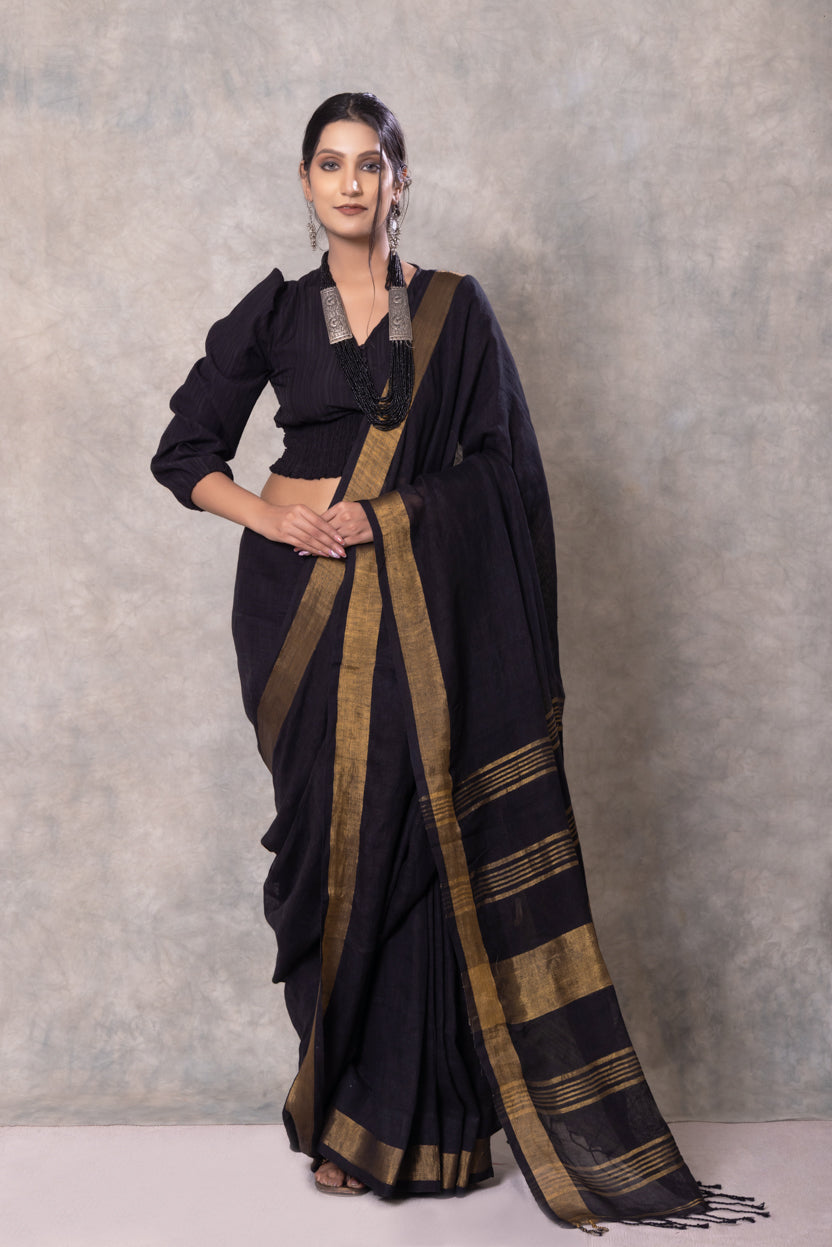 Woman wearing a black saree with gold stripes against a gray background