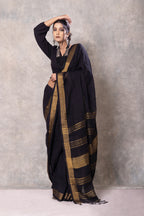 Woman wearing a black saree with gold stripes against a gray background