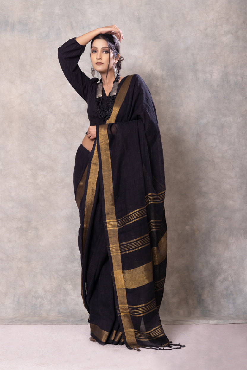 Woman wearing a black saree with gold stripes against a gray background