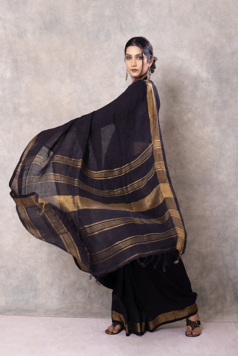 Woman wearing a black and gold saree against a plain background