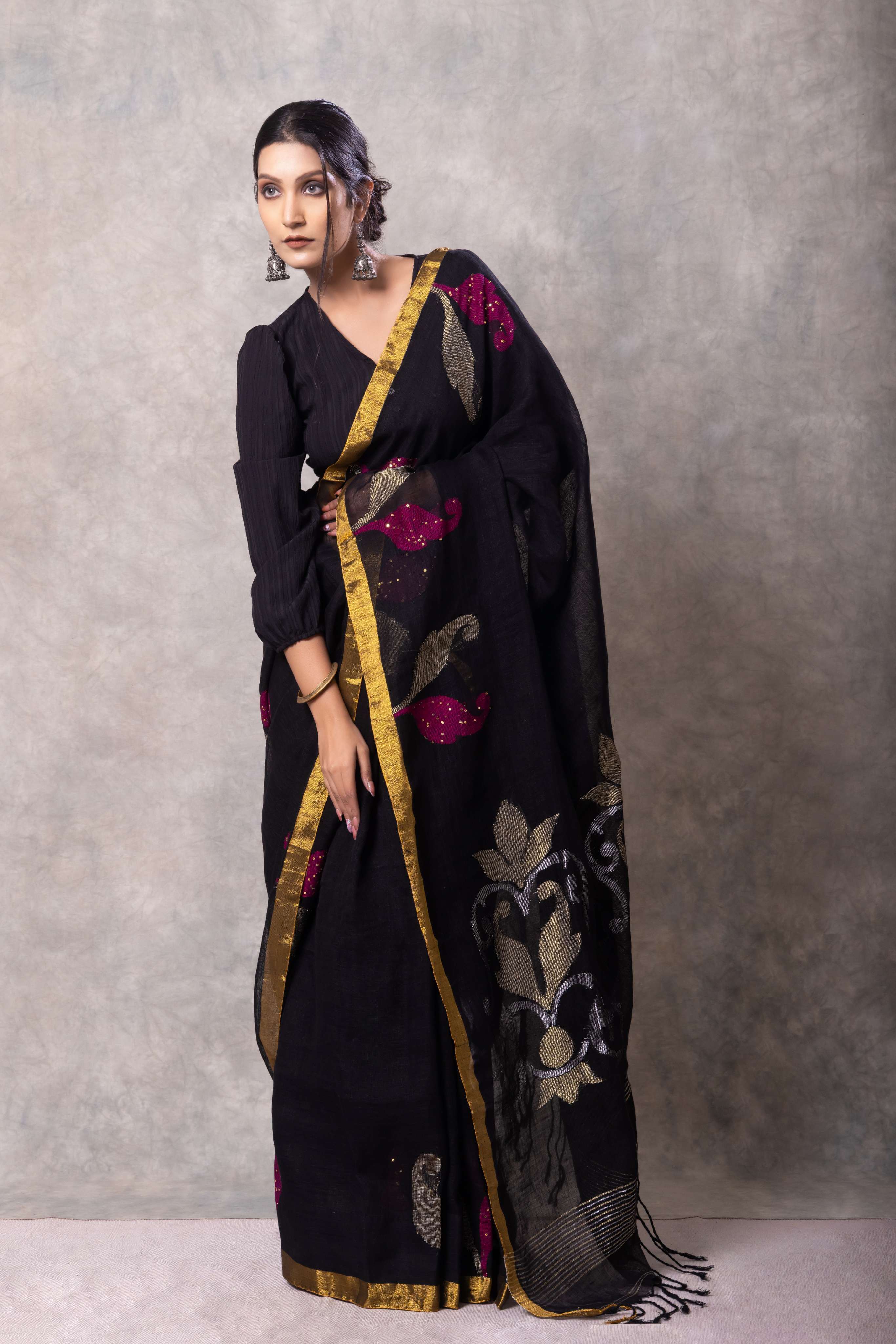 Woman wearing a black saree with gold and pink details against a gray background