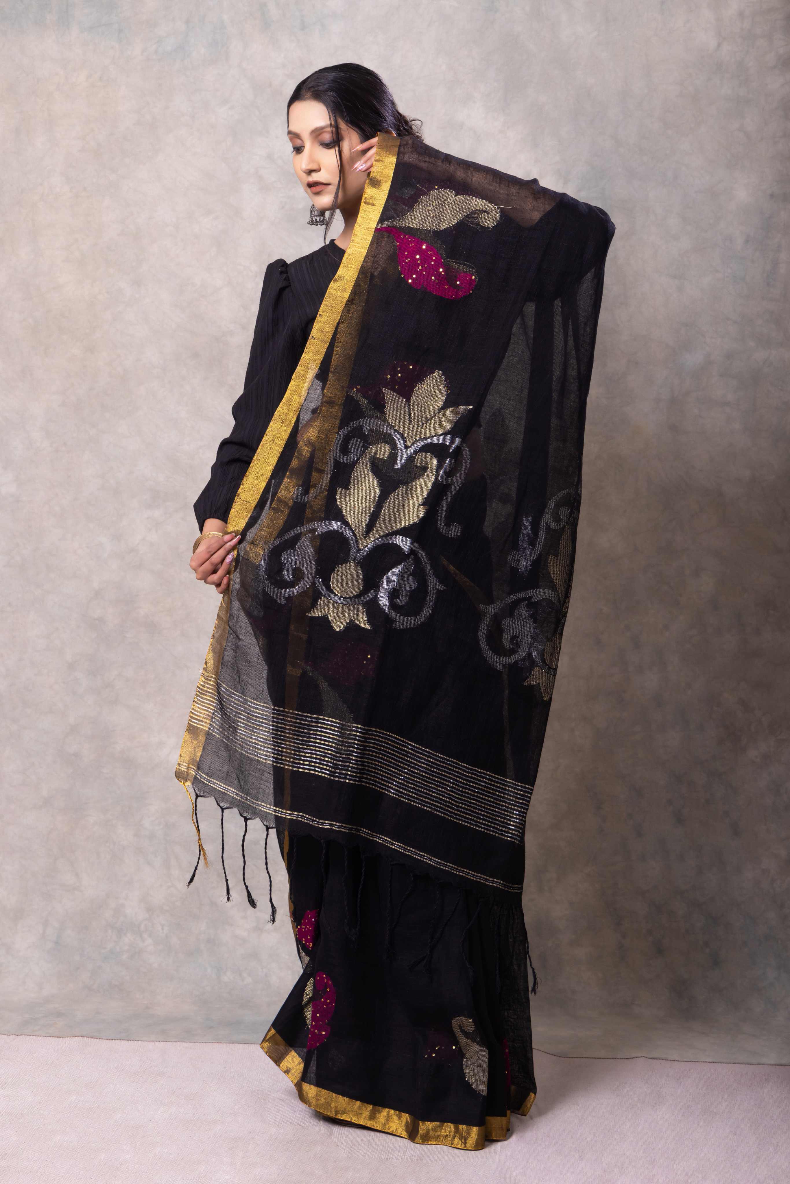 Woman wearing a black saree with floral patterns and embroidery against a gray background