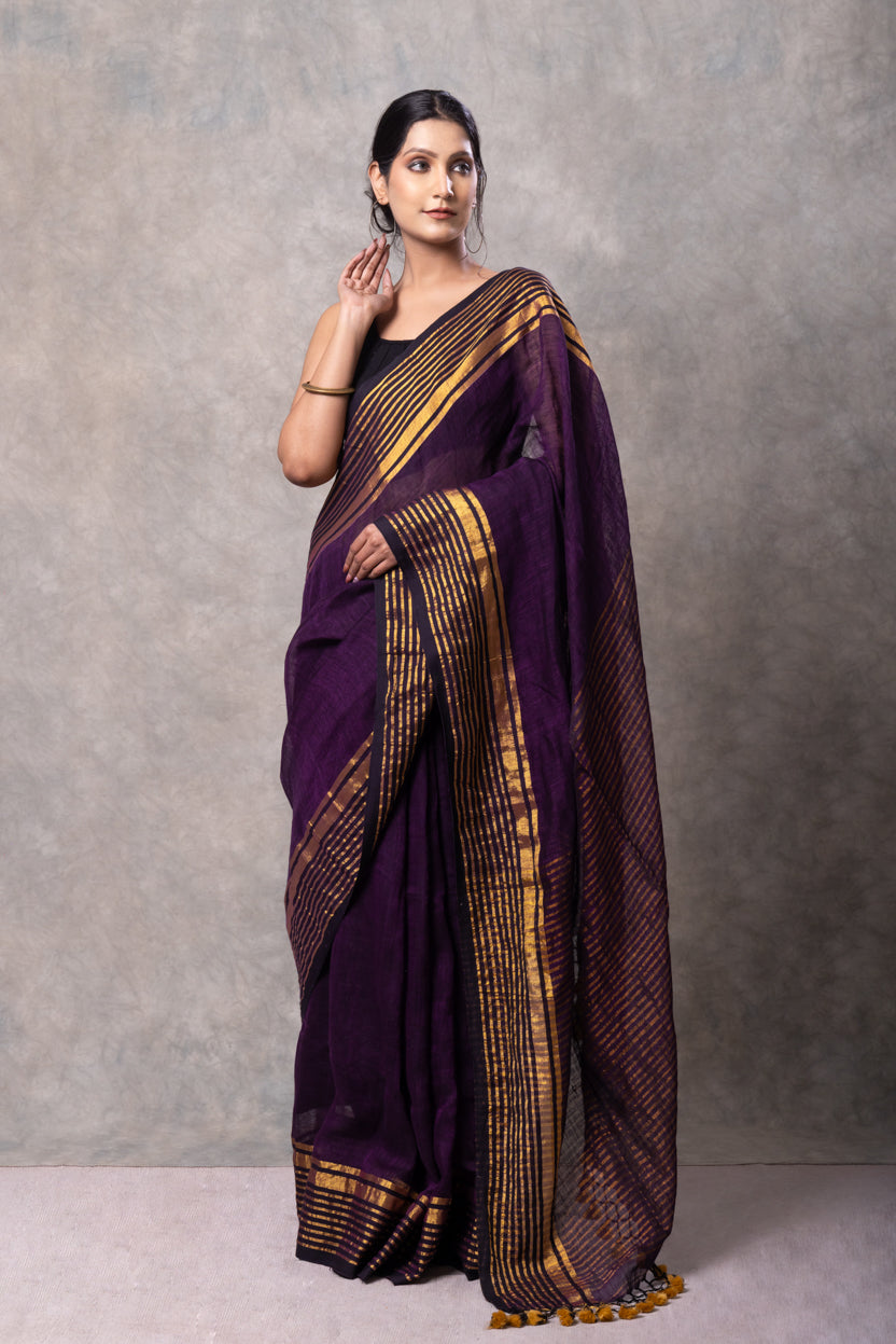Woman wearing a purple saree with gold patterns against a gray background