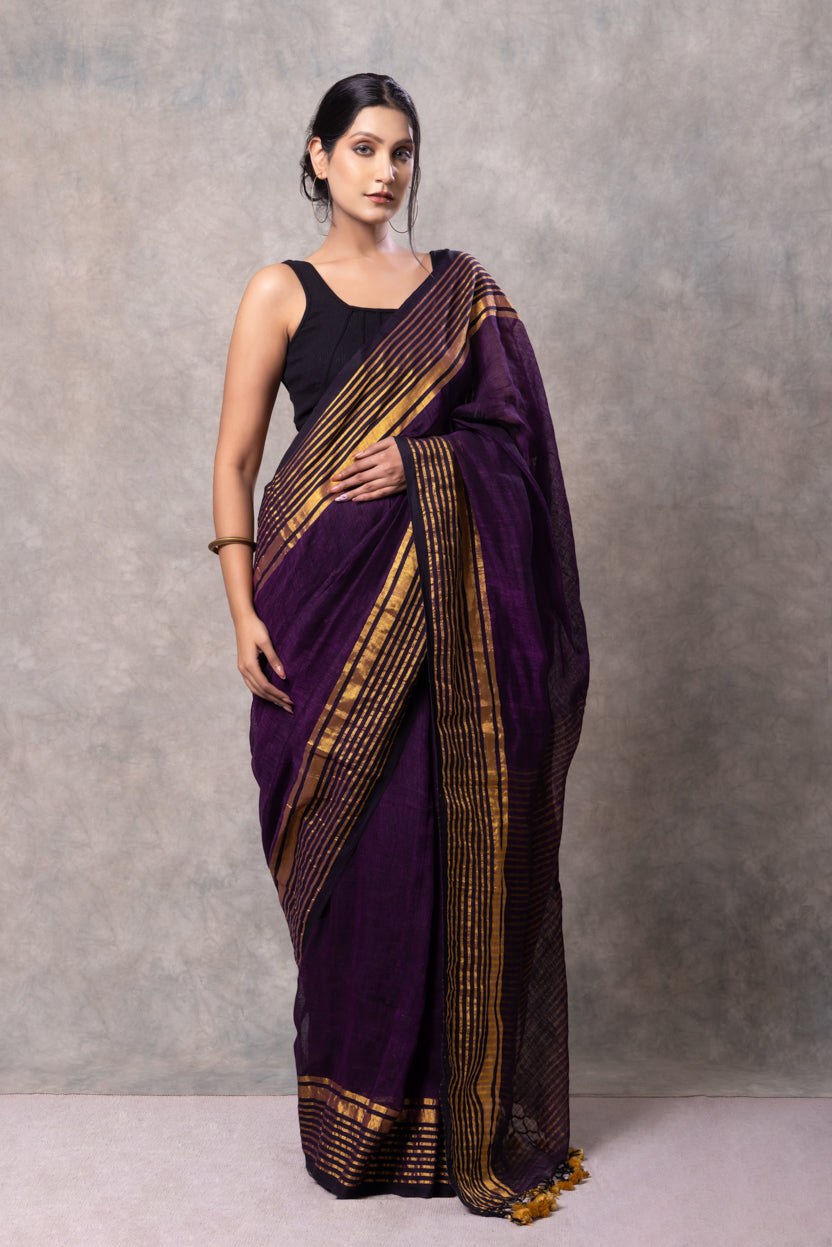 Woman wearing a purple saree with gold border against a gray background