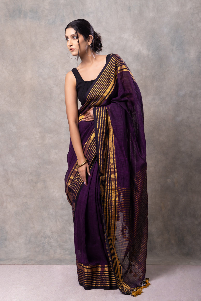 Woman wearing a purple saree with gold patterns against a gray background