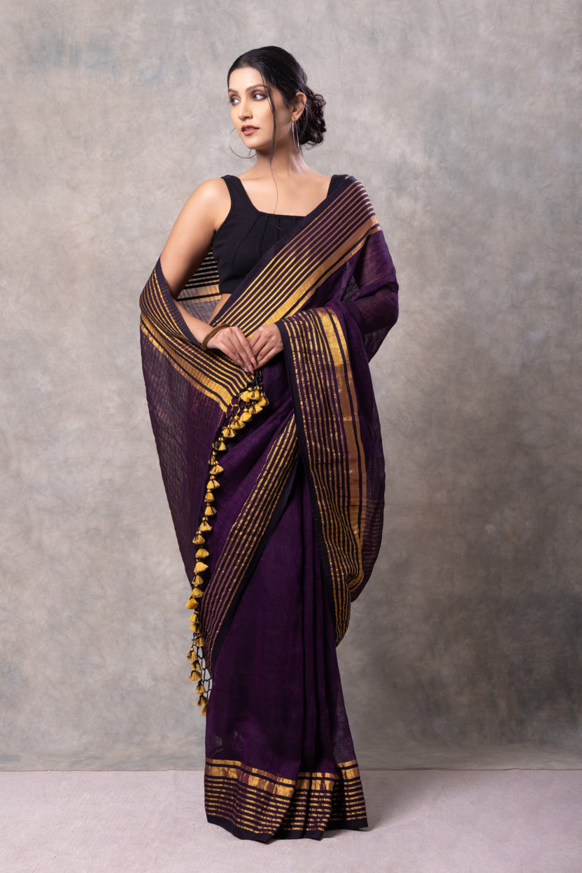 Woman wearing a purple saree with gold border against a gray background