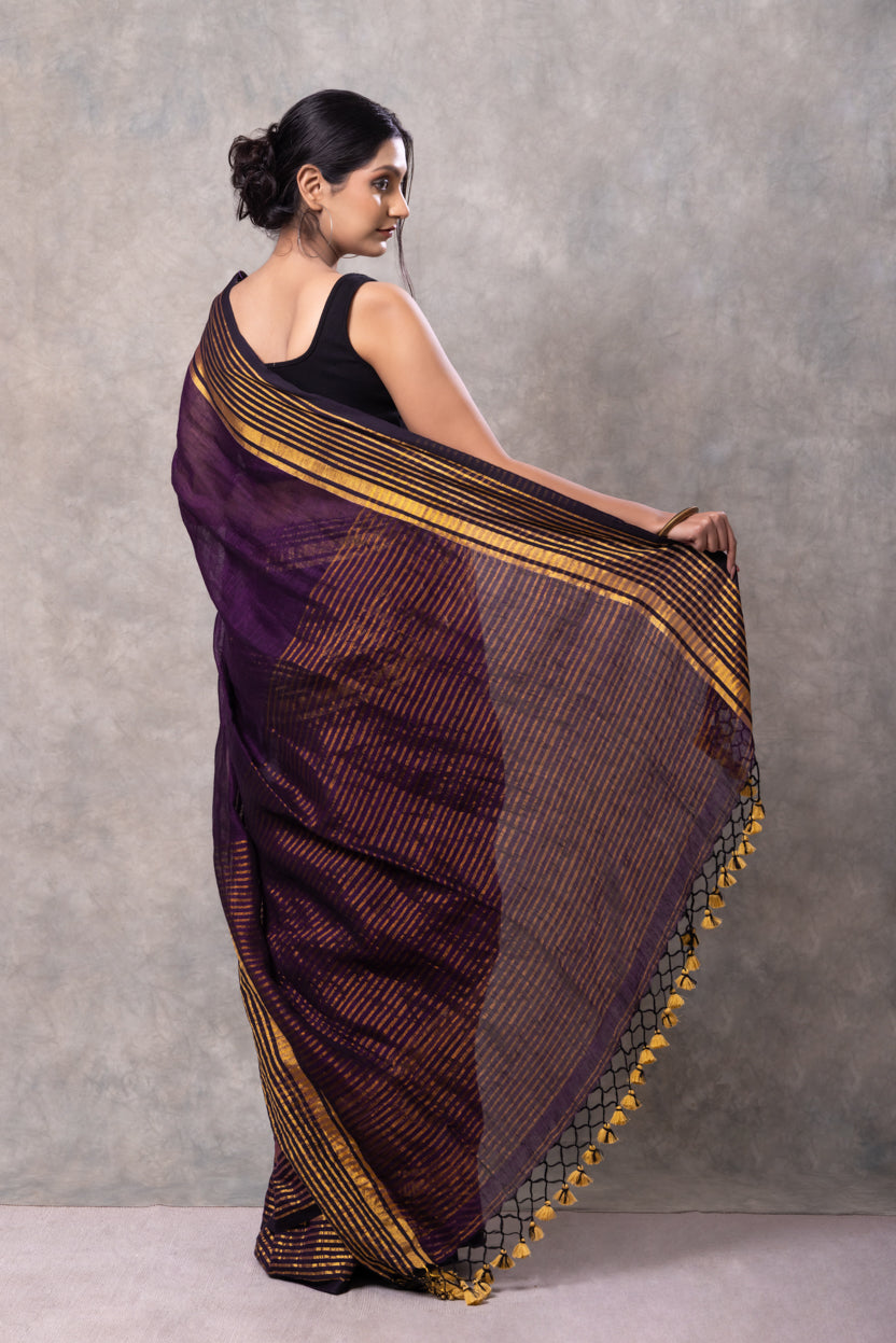Woman wearing a traditional saree with a purple and gold pattern against a gray background