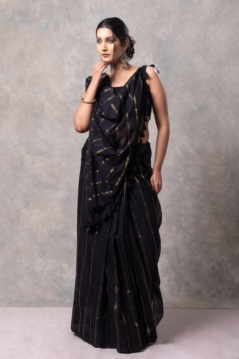 Woman wearing a black saree with gold patterns against a gray background