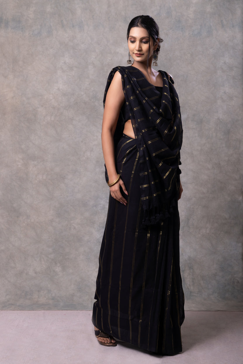 Woman wearing a black saree with gold patterns against a gray background