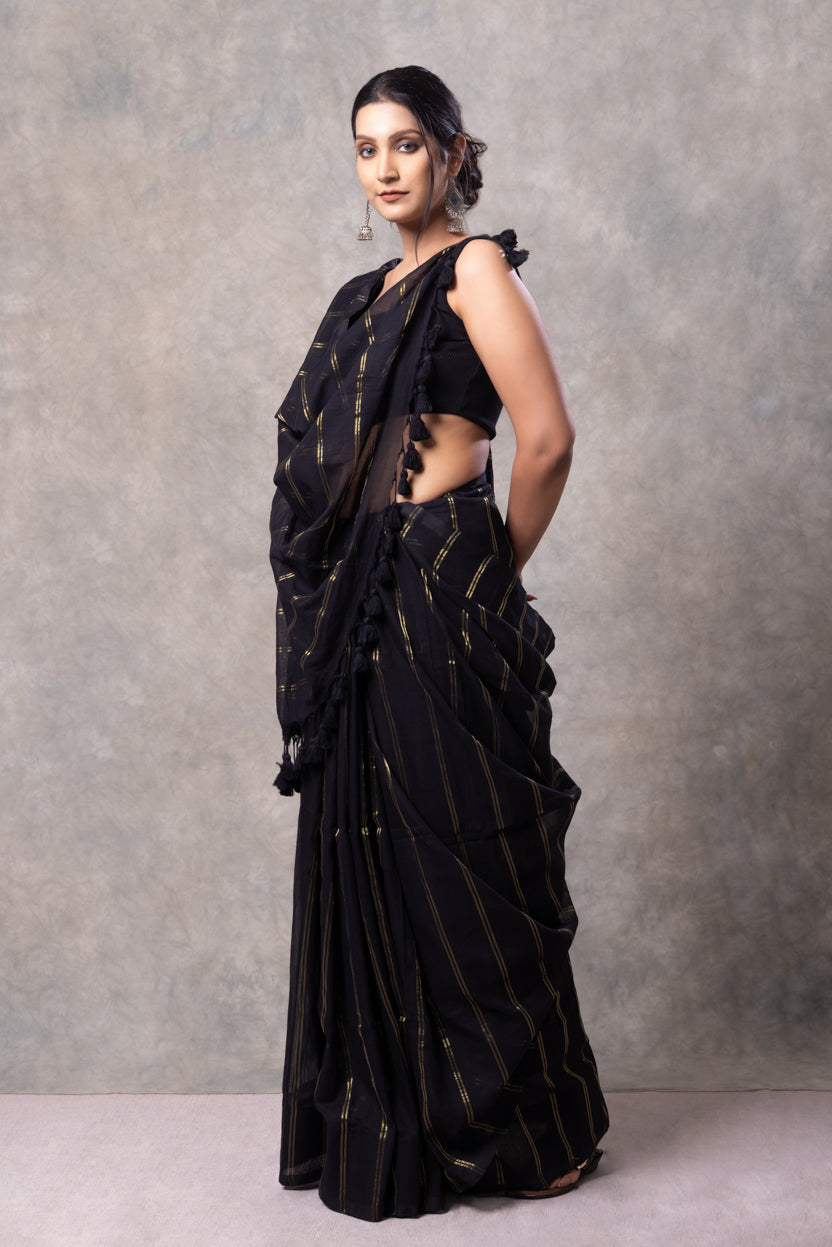 Woman wearing a black saree with gold patterns against a gray background