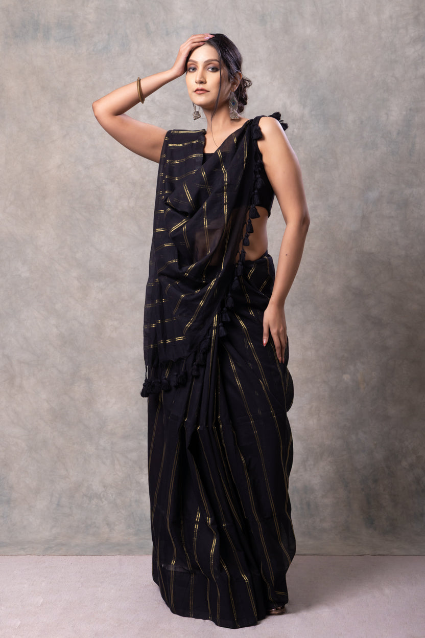 Woman wearing a black saree with gold patterns against a gray background