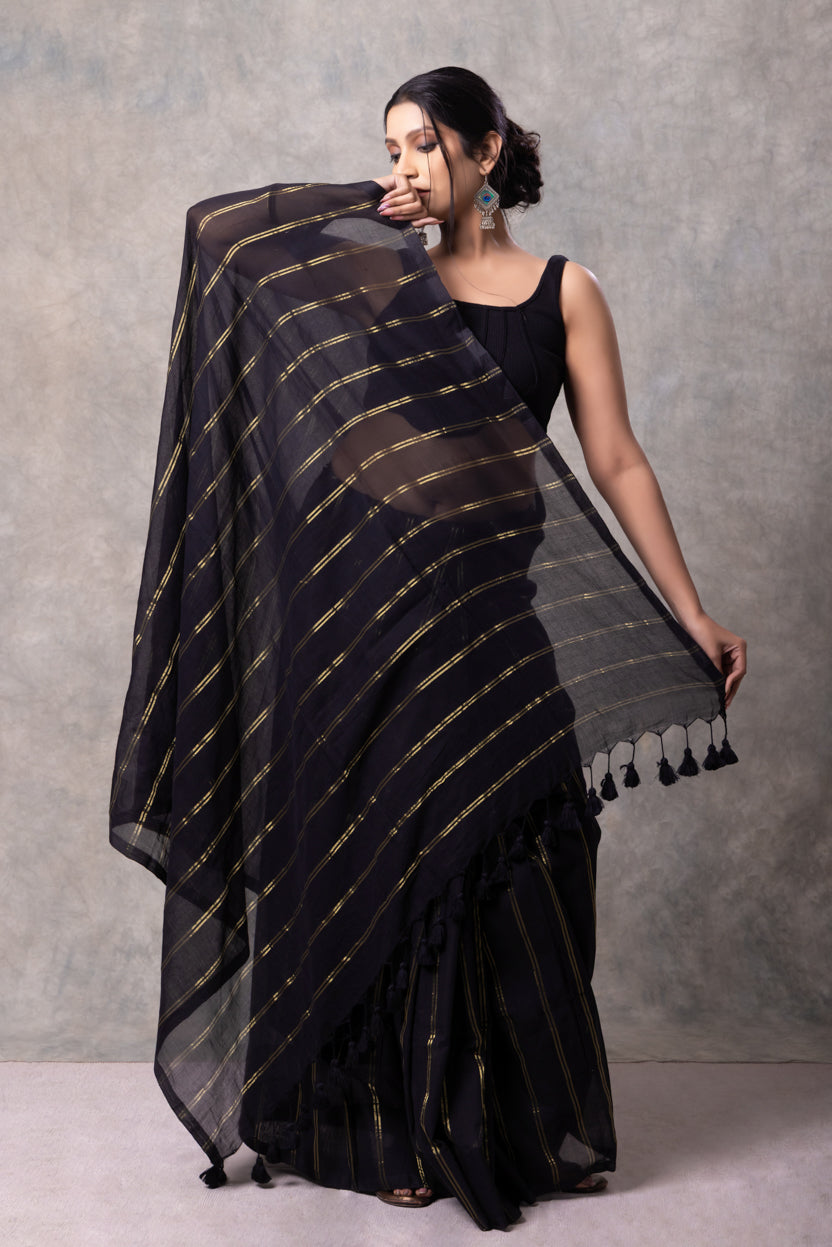 Woman wearing a black saree with gold stripes against a gray background