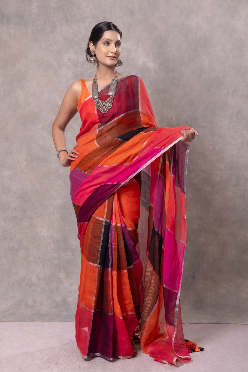 Woman wearing a vibrant orange and pink saree against a plain background