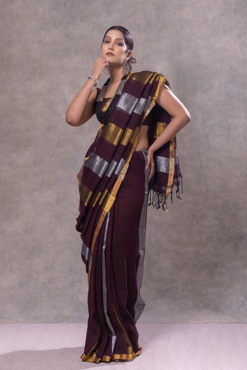 Woman wearing a maroon saree with gold and gray stripes against a plain background