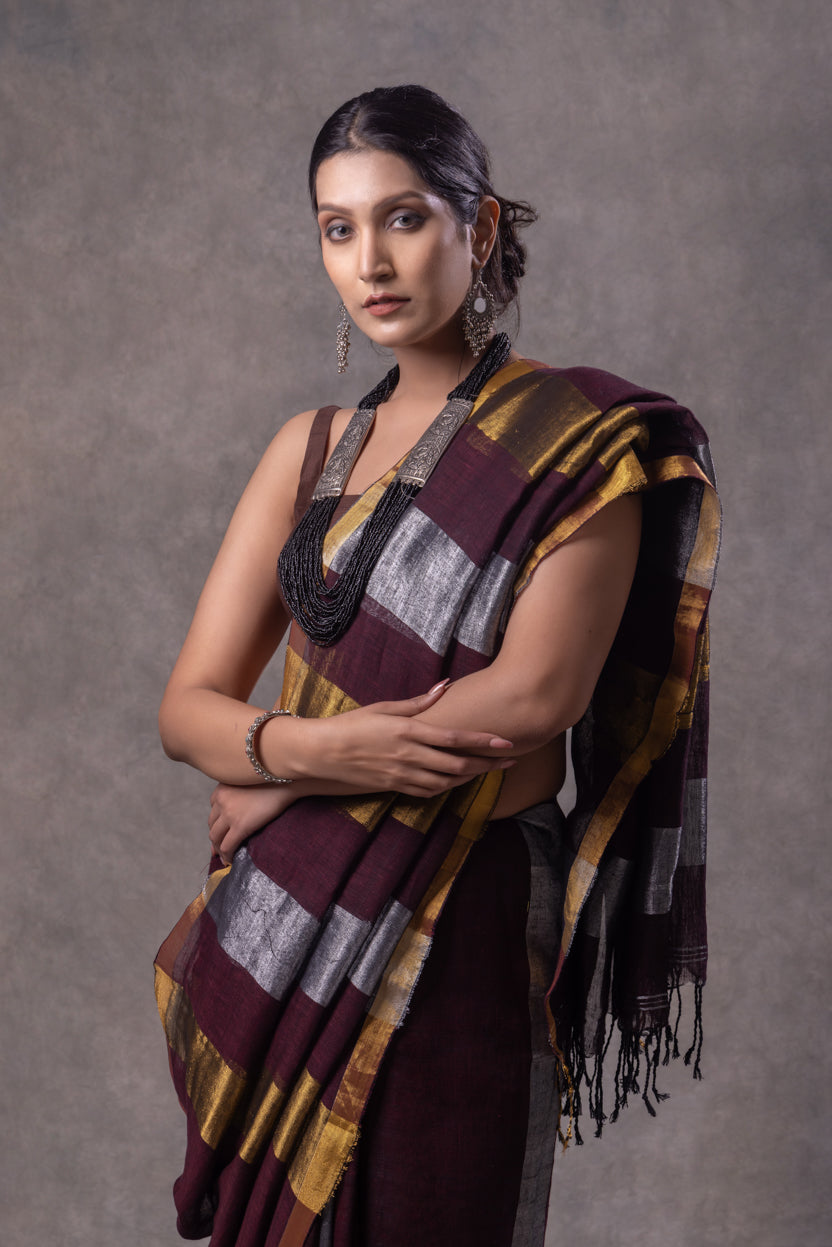 Woman wearing a traditional saree with a maroon and gold pattern against a gray background