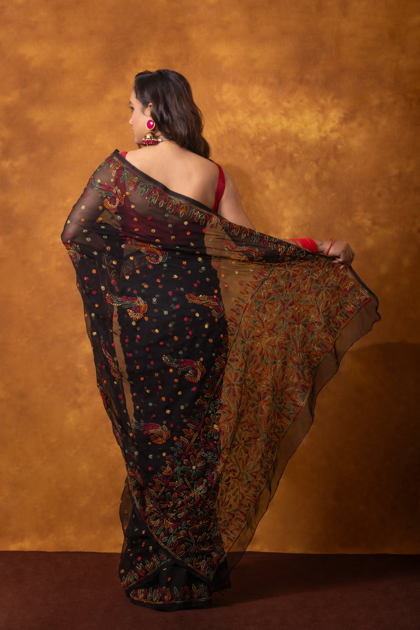 Woman wearing a black floral saree against a brown background