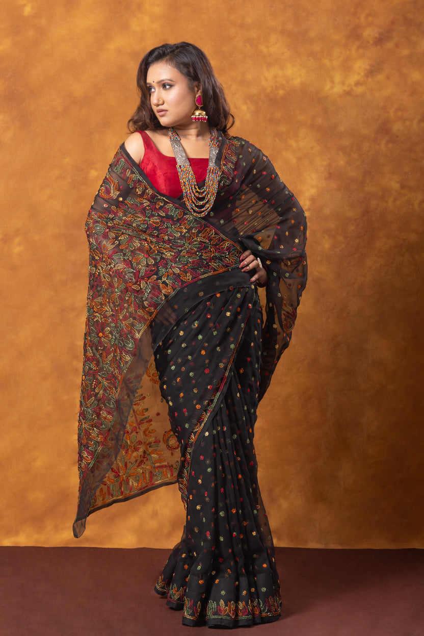 Woman wearing a black saree with a pattern against an orange background