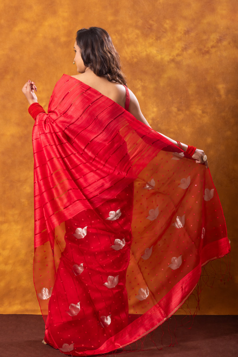 Woman wearing a red saree with white patterns against an orange background