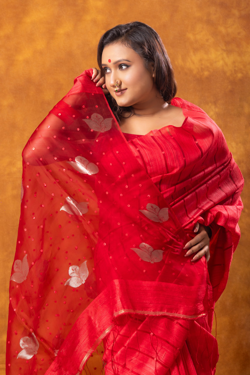Woman wearing a red saree with a floral pattern against an orange background