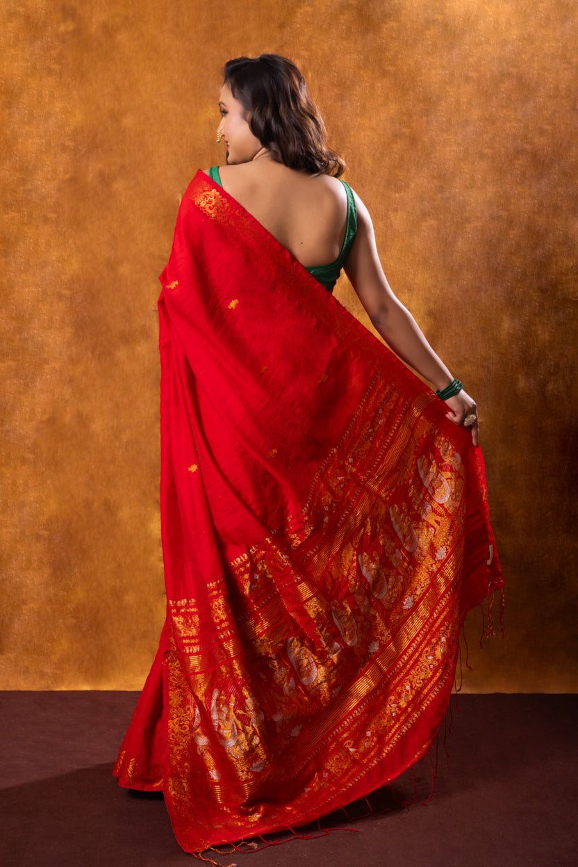 Woman wearing a red saree with gold patterns against a brown background