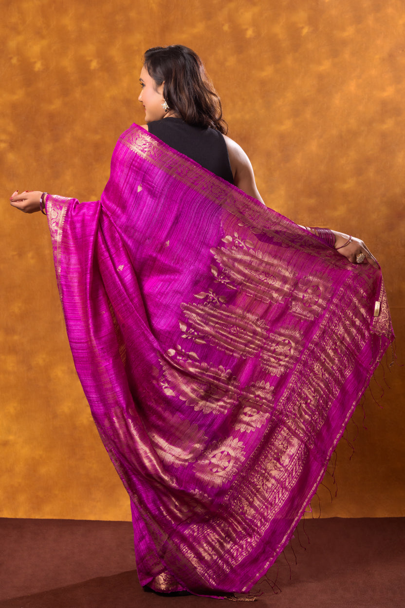 Woman wearing a vibrant purple saree with gold patterns against an orange background