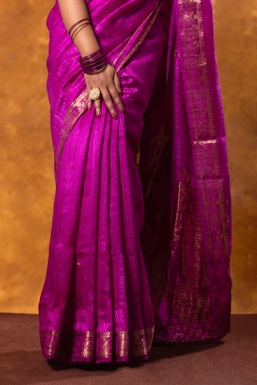 Purple saree with gold border held by a person against a brown background