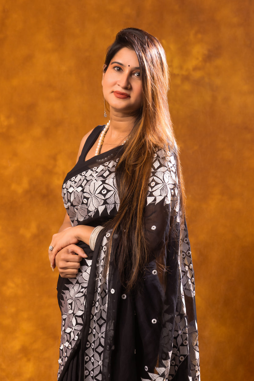Woman wearing a black and white patterned saree against an orange background