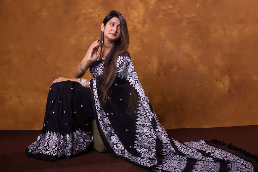 Woman in a black and white floral saree against an orange background