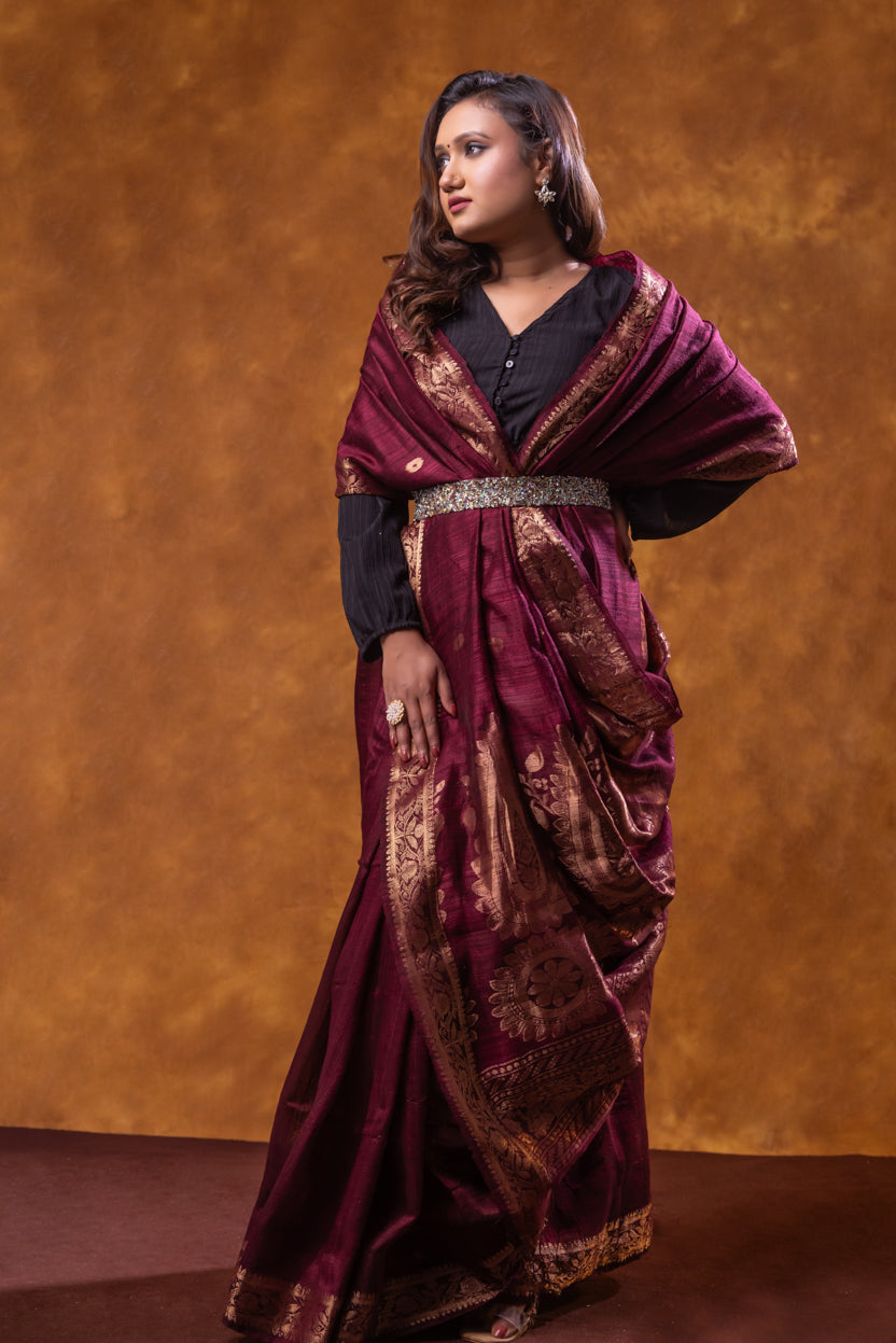 Woman wearing a traditional maroon saree with gold patterns against a brown background