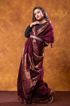Woman wearing a maroon saree with gold patterns against an orange background