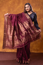 Woman holding a maroon saree with gold patterns against a brown background