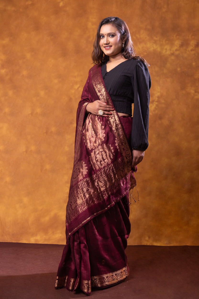 Woman wearing a maroon saree with gold patterns against an orange background