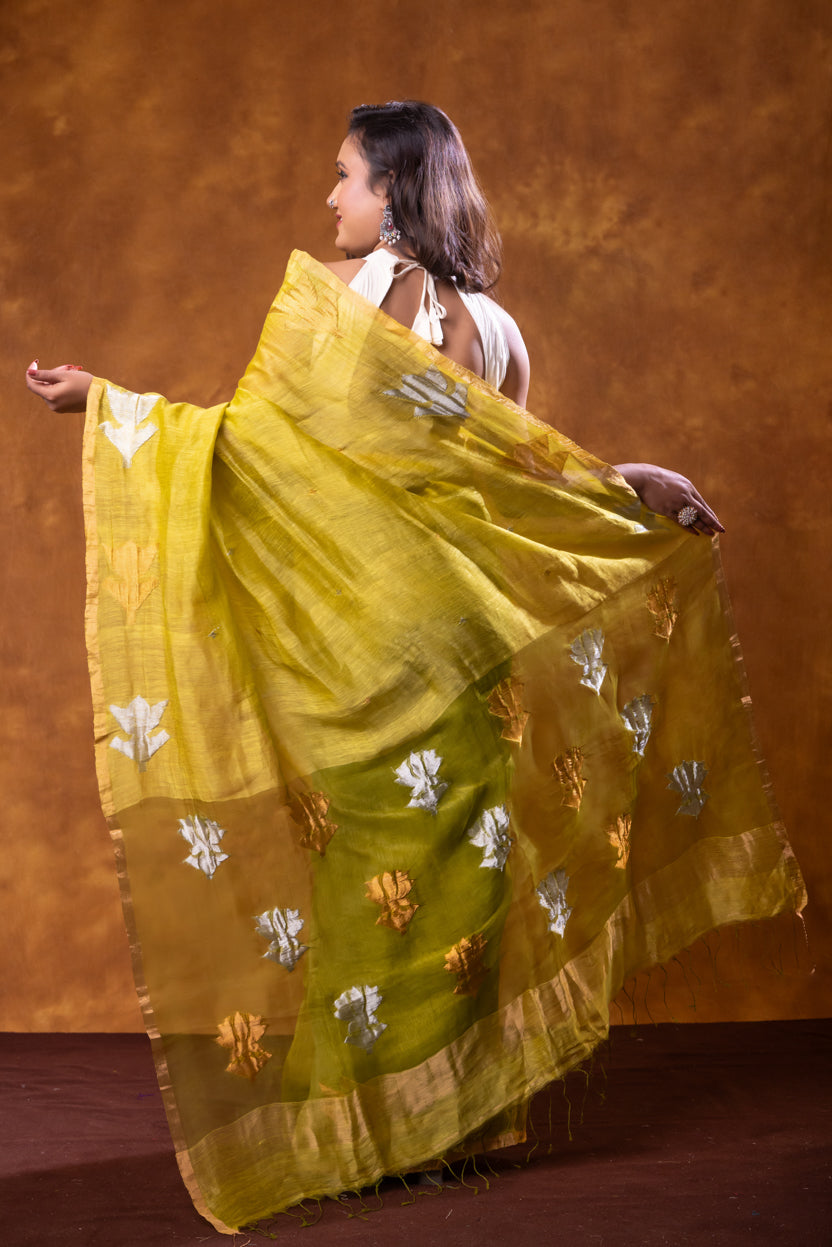 Woman wearing a yellow saree with silver patterns against a brown background