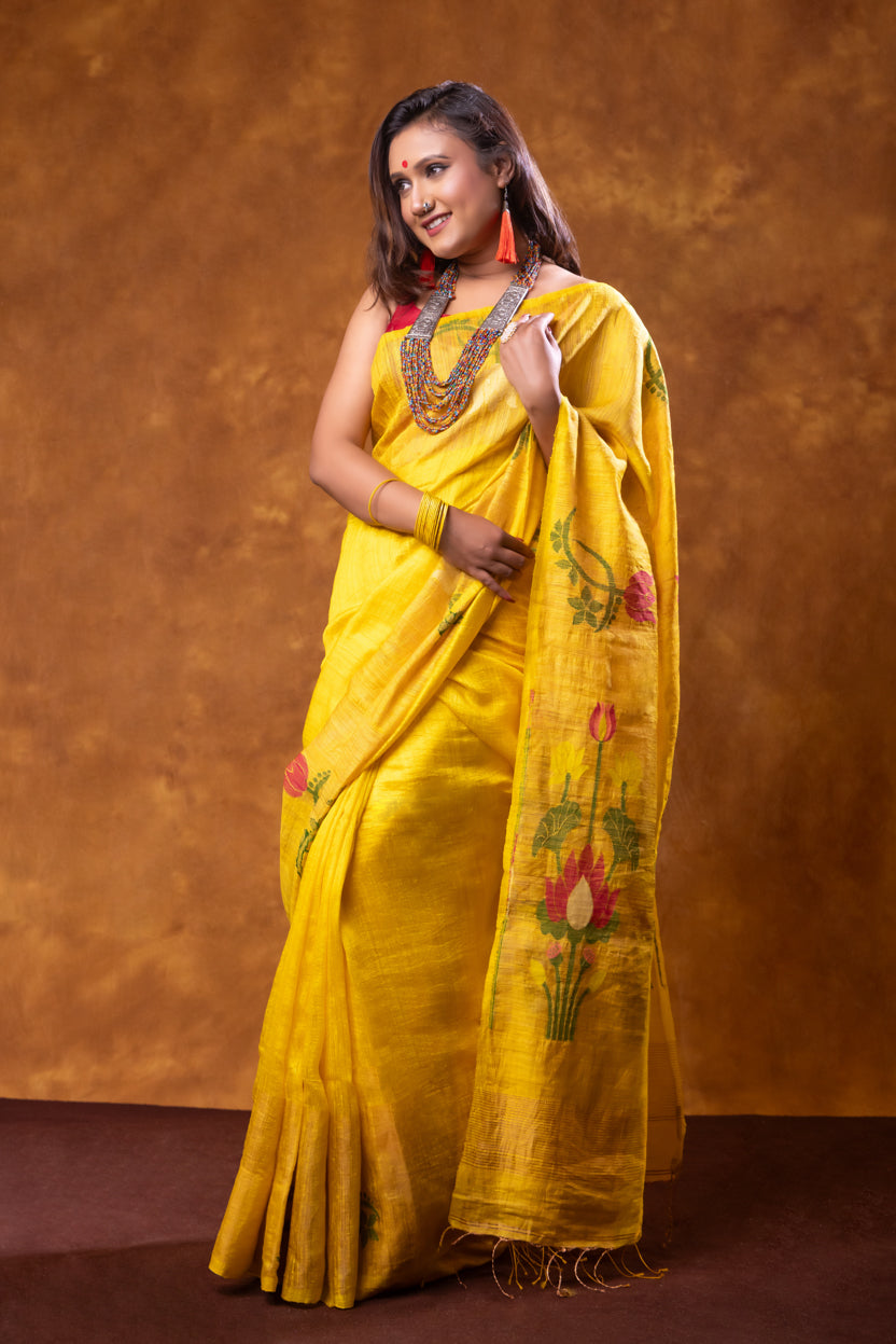 Woman wearing a yellow saree with floral patterns against a brown background