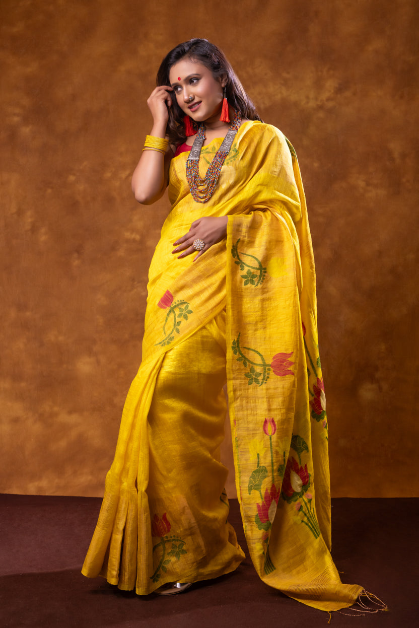 Woman wearing a yellow saree with floral patterns against a brown background