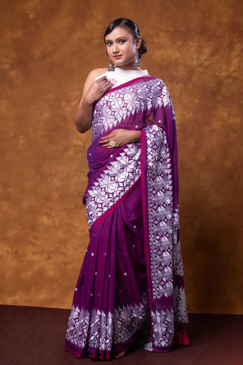 Woman wearing a purple and white saree against a brown background