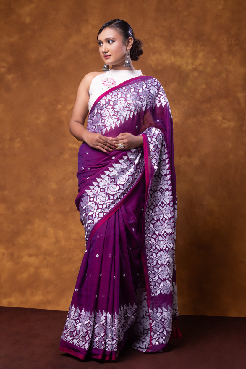 Woman wearing a purple and white saree against a brown background