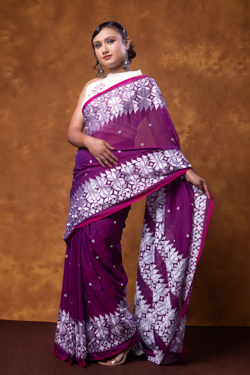 Woman wearing a purple and white saree against a brown background