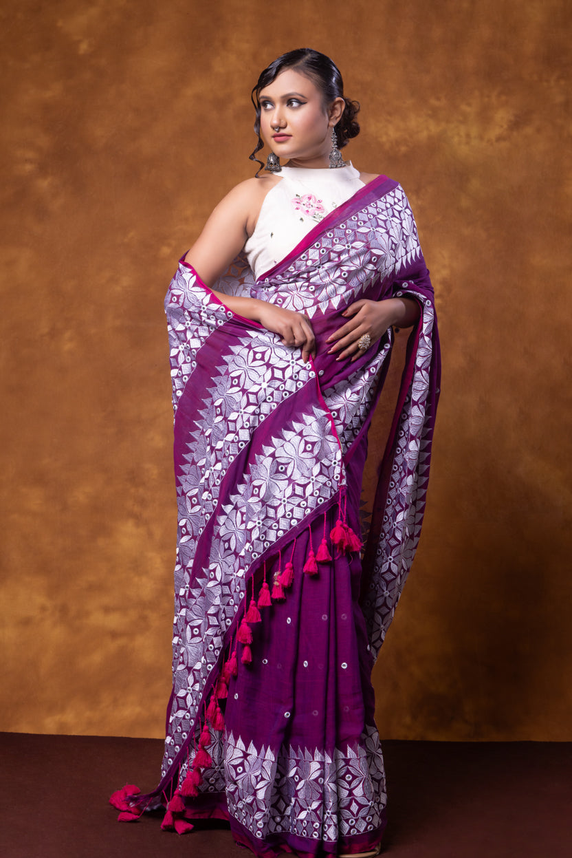 Woman wearing a purple and white saree with a brown background
