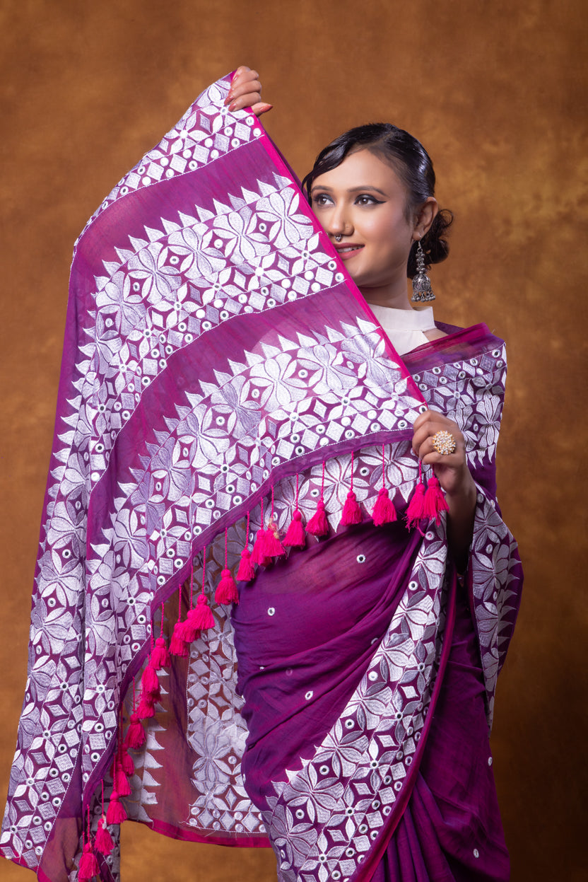 Woman holding a purple saree with pink tassels against a brown background